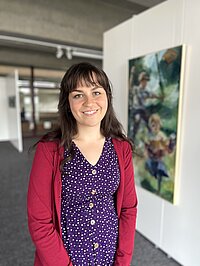 Porträtfoto: Die Masterstudentin Eliška Strnadová, im Hintergrund unscharf ihr Gemälde in der Kunstschau