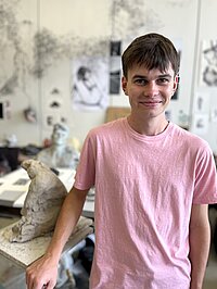 junger Mann mit rosa t-Shirt im Atelier, lächelnd in die Kamera blickend