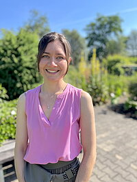 Porträt: junge Frau, lächelnd, mit pinkem, kurzärmeligen Top, im freien aufgenommen im botanischen Garten